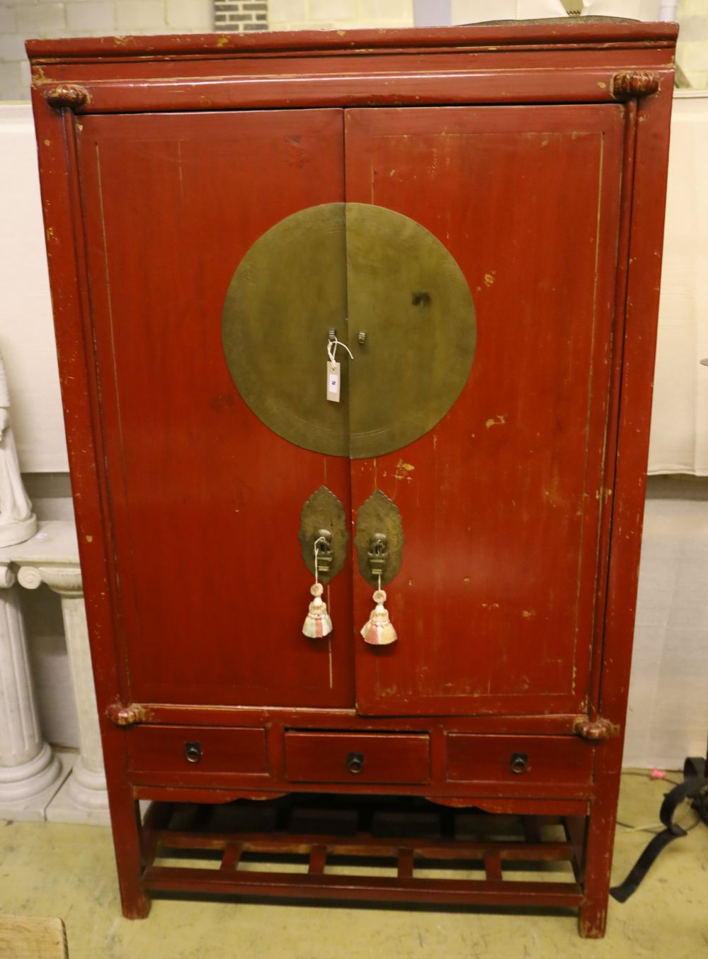 A Chinese two-door brass-mounted red-lacquered cupboard fitted three short drawers over an open shelf, width 110cm, depth 60cm, height